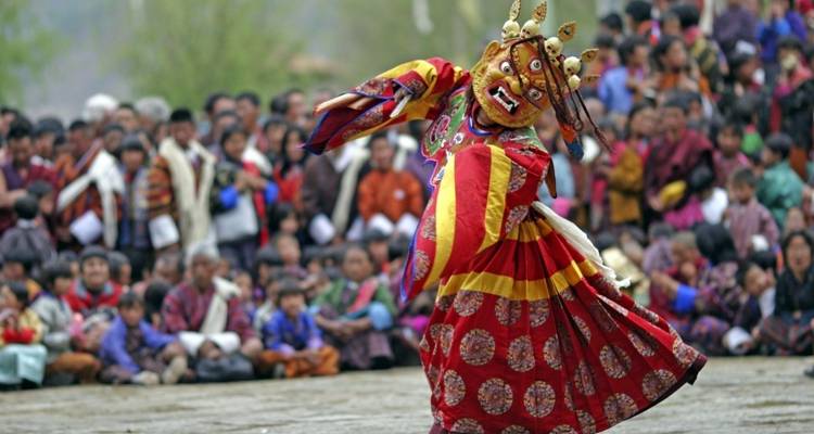 Traditional Bhutanese dance performance with a masked dancer and an audience.
