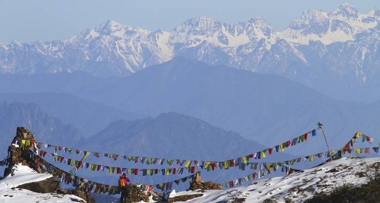 Himalayan mountain range with prayer flags and ruins on a snowy hill.