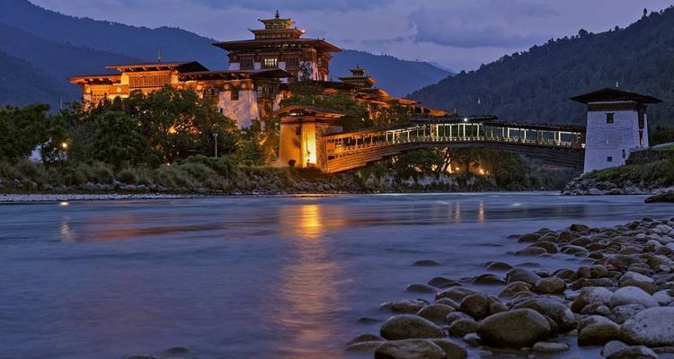 Punakha Dzong lit up at night with a river in the foreground.