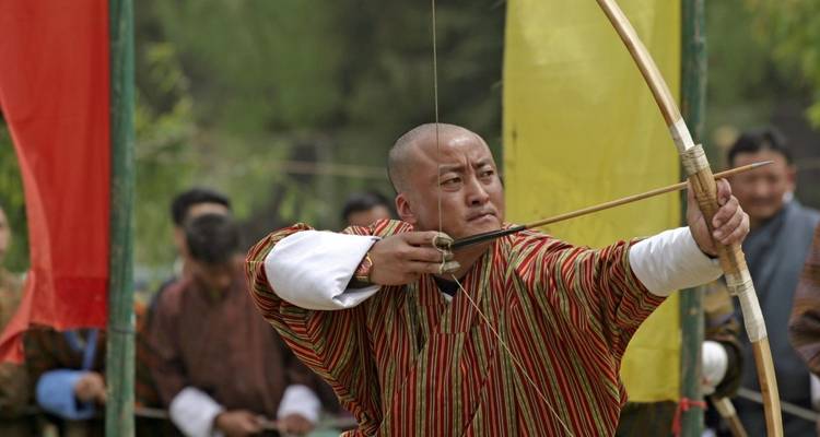 Traditional archer aiming at a target with spectators in the background.