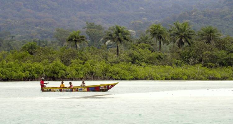 Menschen in einem kleinen Boot auf einem Fluss mit Palmen im Hintergrund.