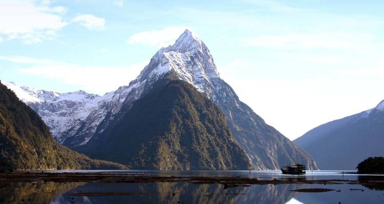 Mitre Peak and surrounding mountains reflected in a calm fjord.