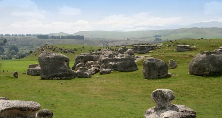 Rock formations in a grassy field with hills in the background.