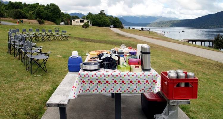 Picnic setup on a table with a lake and mountains in the background.