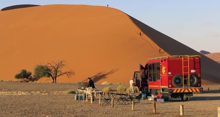 Desert camping scene with a red truck and large sand dune.