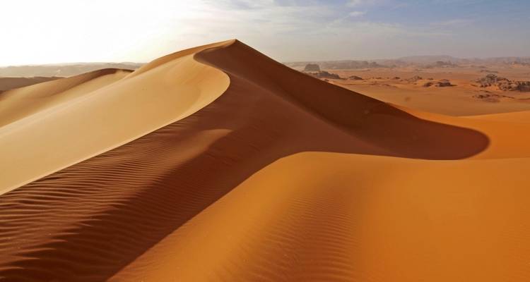 Une grande dune de sable aux courbes douces et ondulations se détachant contre le ciel.