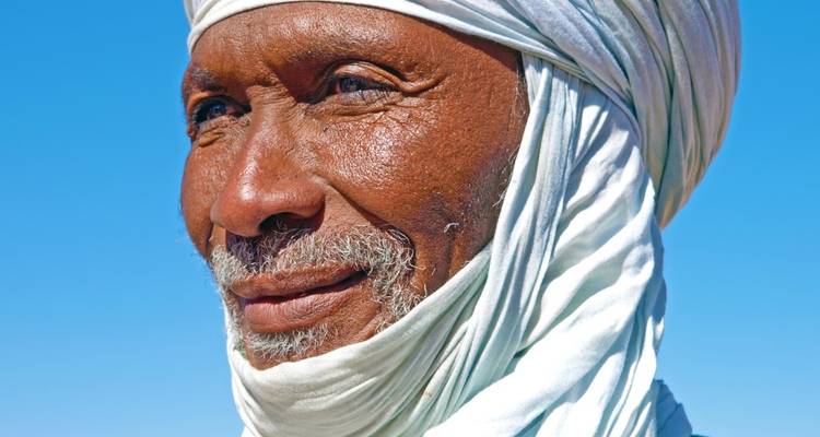 Portrait d'un homme portant un turban blanc, sur fond de ciel bleu clair.