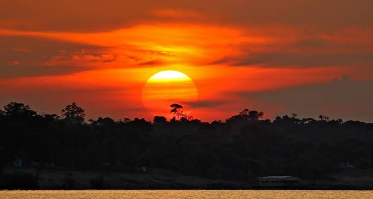 Vibrant sunset over a river with trees silhouetted.