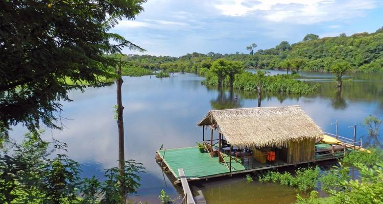 Thatched hut on a raft surrounded by lush greenery and a water body.