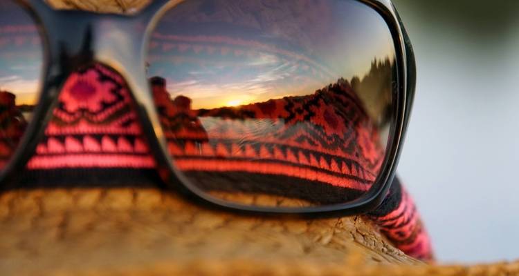 Sunglasses reflecting a scenic sunset with patterned fabric.
