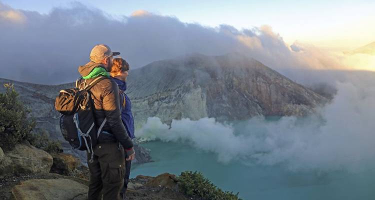 Pareja mirando paisaje volcánico con neblina elevándose de un cráter en Indonesia.