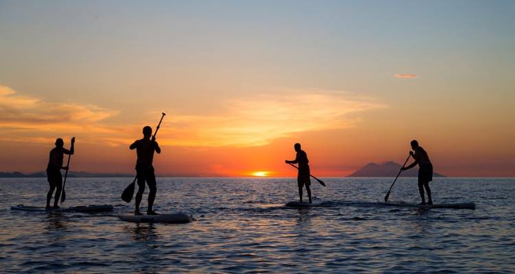Silhouetten van mensen die paddleboarden tijdens een kleurrijke zonsondergang.