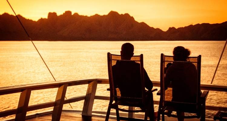Twee mensen die op stoelen zitten en genieten van een zonsonderganguitkijkje over het water.
