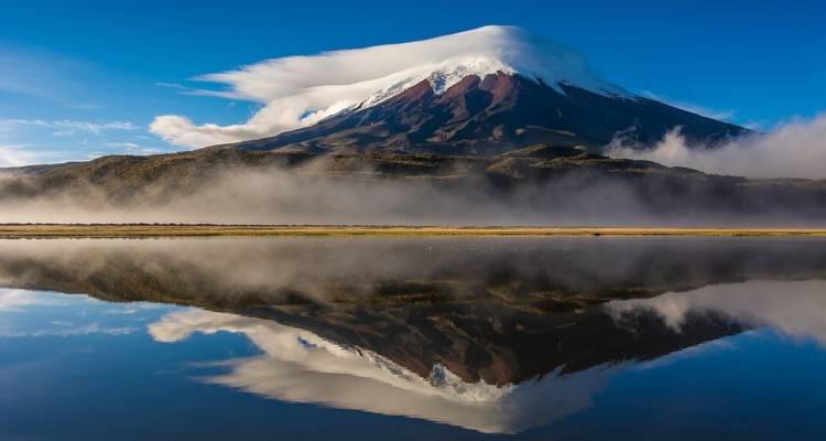 Reflection of a snow-capped volcano in a lake with mist.