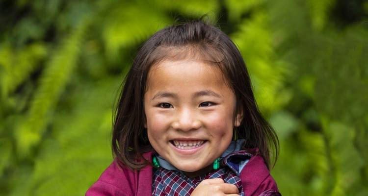 A smiling child against a foliage backdrop.