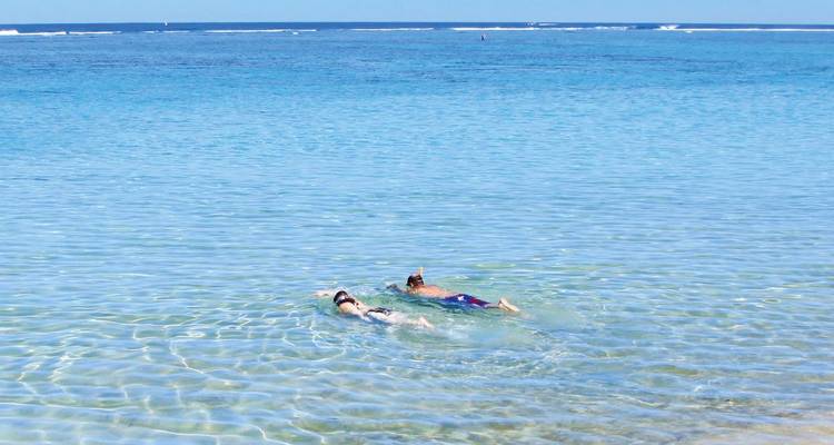 Deux personnes faisant de la plongée avec tuba dans une eau océanique bleue et cristalline.