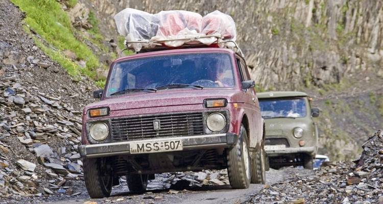 Vehículos viejos transportando mercancías por una carretera montañosa accidentada.