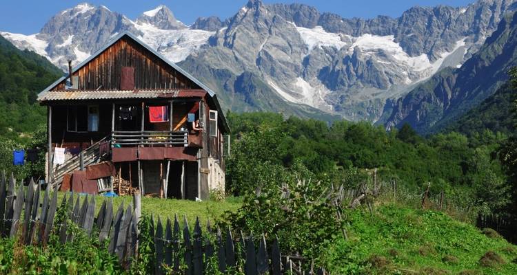 Casa de madera en un valle verde y frondoso con montañas al fondo.