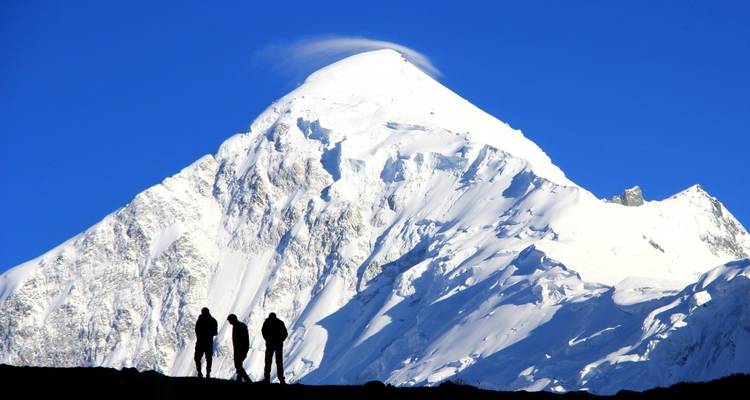 Gesilhouetteerde trekkers tegen een besneeuwde bergtop.