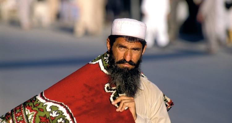 Man in traditionele kleding die een tapijt draagt.