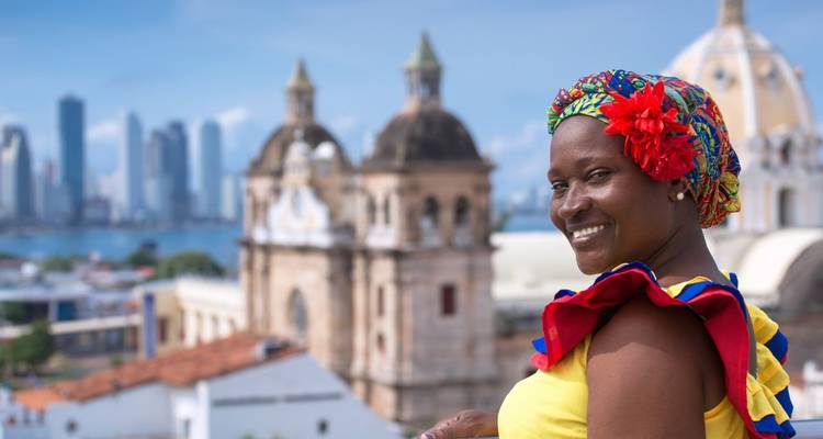 Eine lächelnde Frau in traditioneller Kleidung mit einer Stadtskyline im Hintergrund.