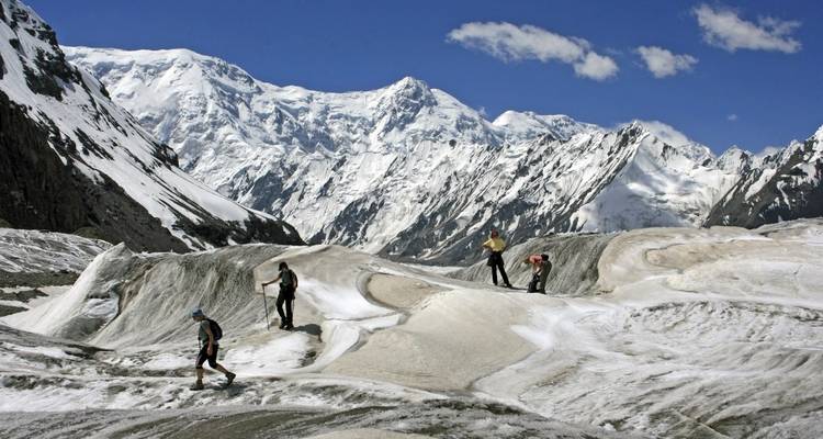 Group of hikers traversing a glacier against a backdrop of high mountains.