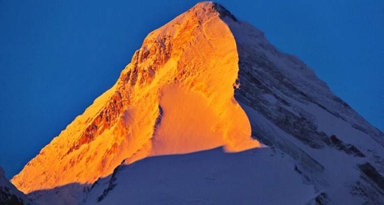 Golden-lit snow-capped mountain peak against a blue sky.