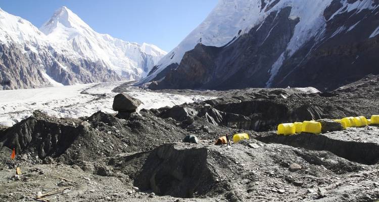 Snowy mountains and camping tents scattered on rocky terrain.