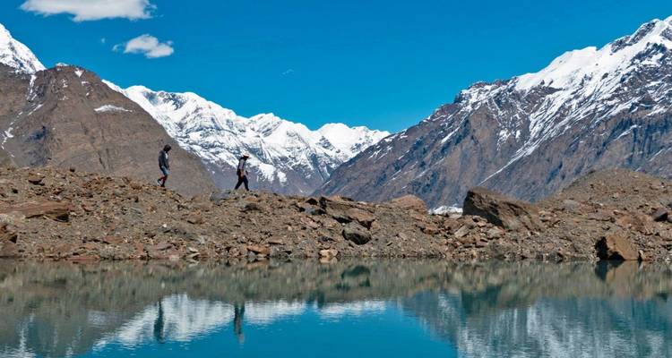 Two hikers walking by a lake with snowy mountains in the background.