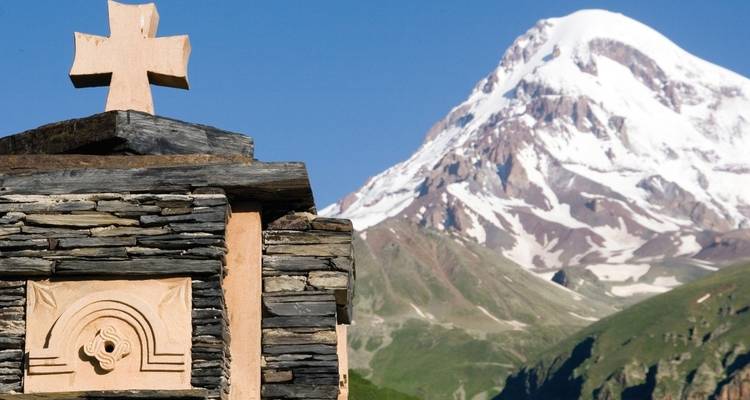 Monument de croix en pierre avec une montagne enneigée en arrière-plan.