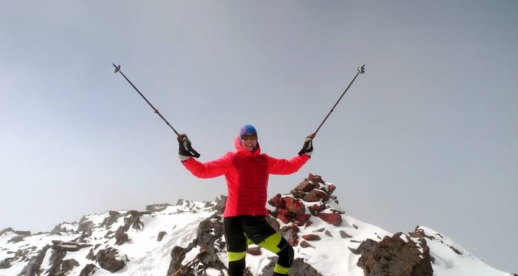Person feiert auf einem schneebedeckten Berggipfel mit erhobenen Wanderstöcken.