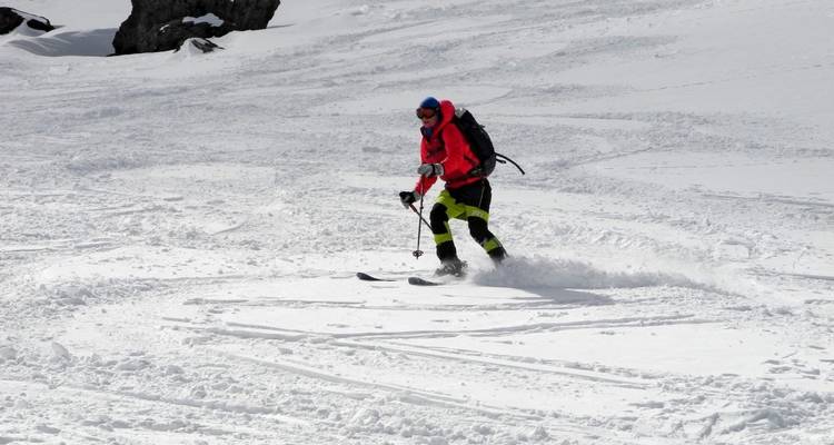 Person, die auf einem verschneiten Berghang bei klarem Himmel Ski fährt.