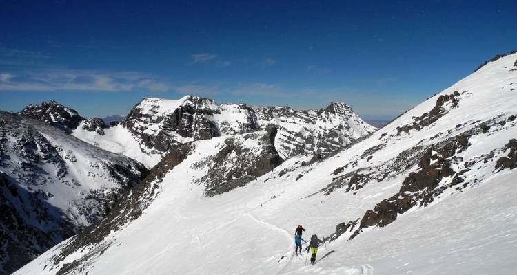 Skifahrer, die einen verschneiten Berghang mit unwegsamem Gelände durchwandern.