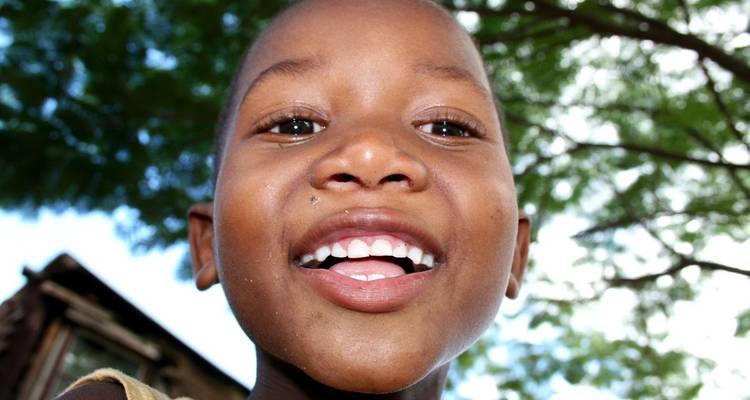 Close-up of a smiling child outdoors under a tree.