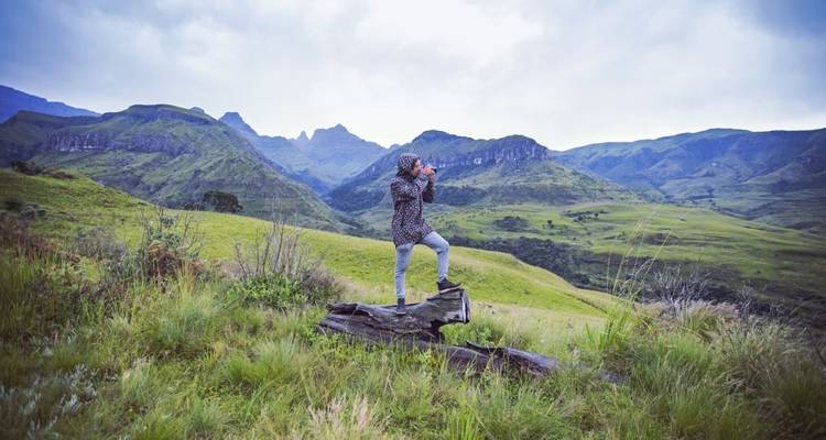 Young hiker standing on a log looking over a valley landscape.