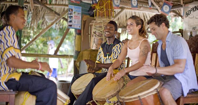 Grupo de personas tocando tambores bajo un techo de paja.