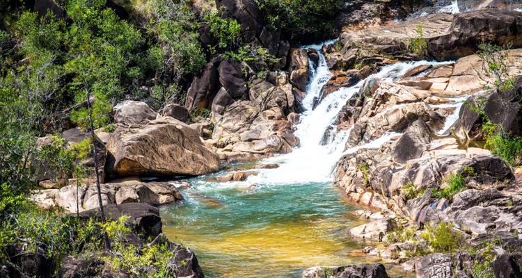 Una pequeña cascada que fluye hacia una piscina cristalina rodeada de rocas.