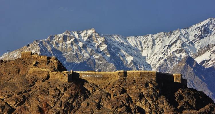 Kharphocho Fort on a rocky hill with snow-covered mountains in the background.