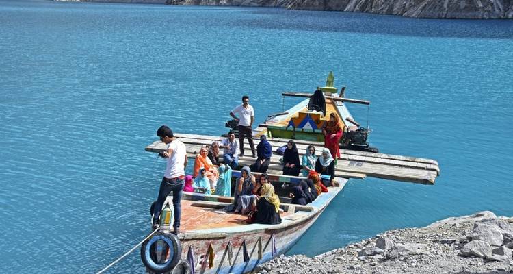 Group of people on a decorated boat in clear blue water near rocky shores.