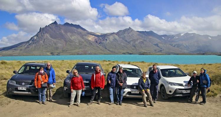 Groep mensen die bij auto's staan met bergen op de achtergrond.