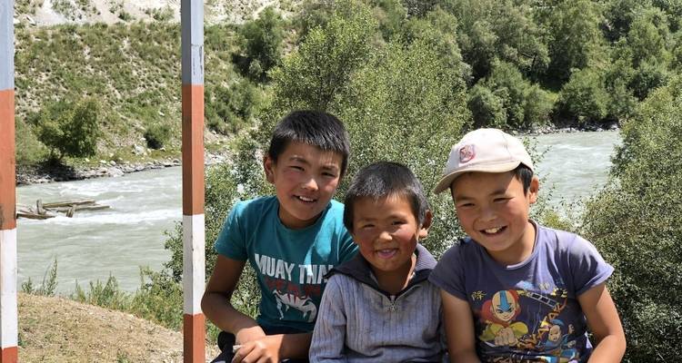 Three boys smiling near a river with trees around.