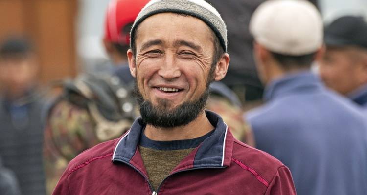 Portrait of a smiling man wearing a cap in a bustling area.
