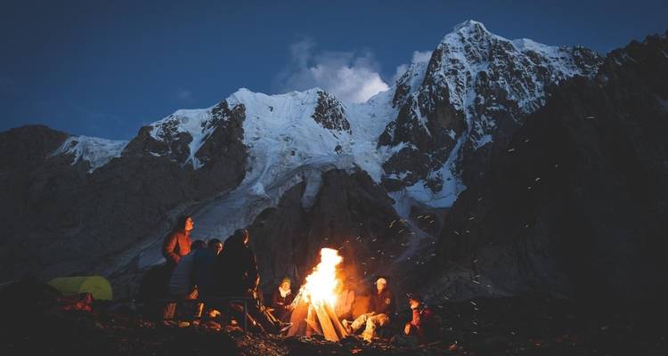 Group gathered around a campfire with snowy mountains in the background.