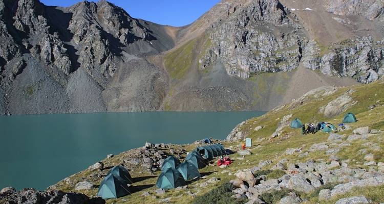 Campsite with tents by a turquoise lake surrounded by rocky mountains.