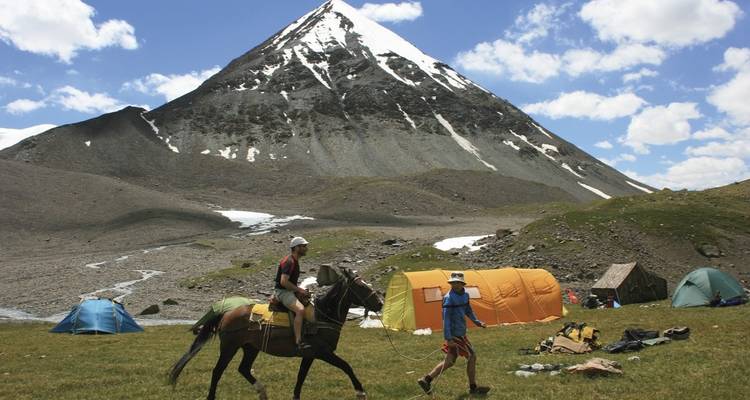 Man on horseback near a campsite with a mountain.
