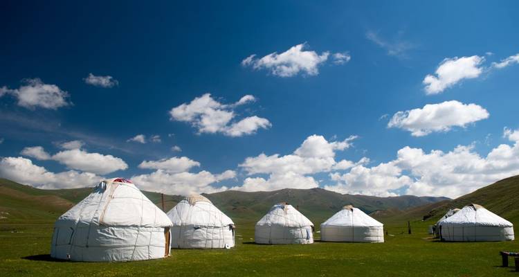 Traditional yurts in a vast open field with blue skies and mountains in the background.