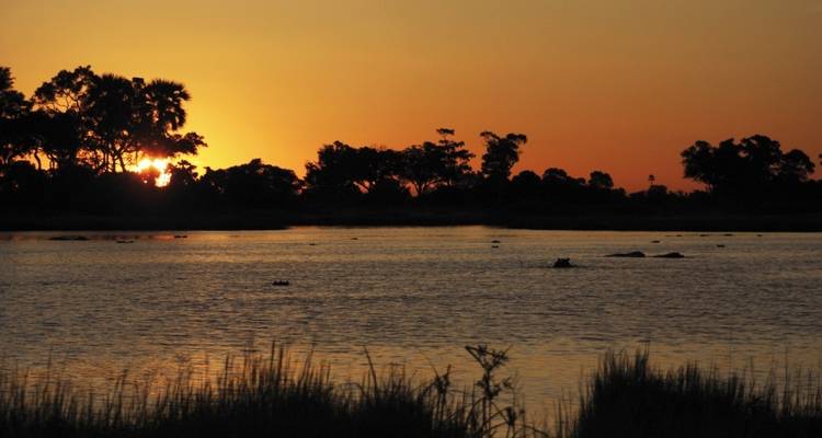 Lago al atardecer con árboles en silueta y reflejos.