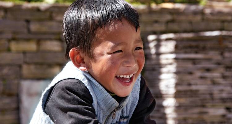 Smiling child dressed warmly, possibly in a rural setting in Nepal.