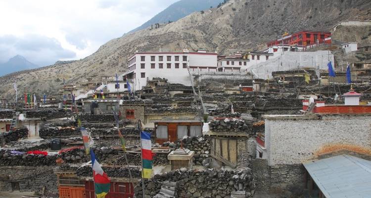 Scenic view of a village with stone houses and colorful flags in a mountainous area.