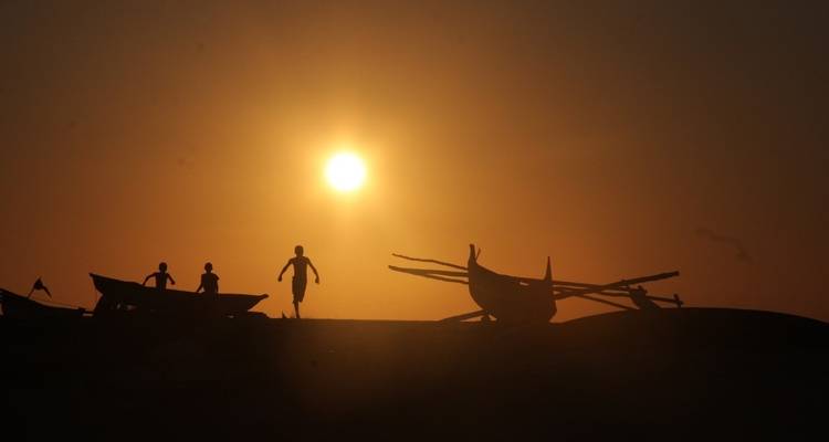 Silhouet van mensen en boten tegen een zonsondergang.